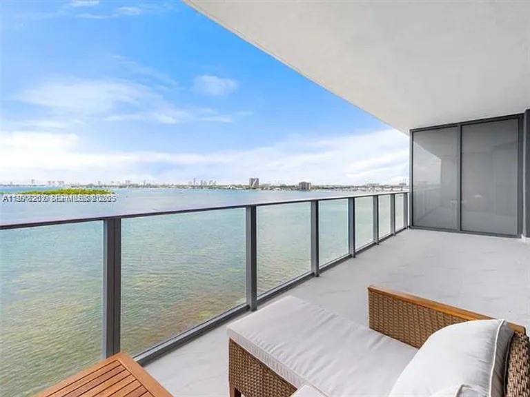 A balcony with a lounge chair overlooks a large body of water and a city skyline — 700 NE 24TH ST # 606, Miami FL 33137, MIAMI, FL