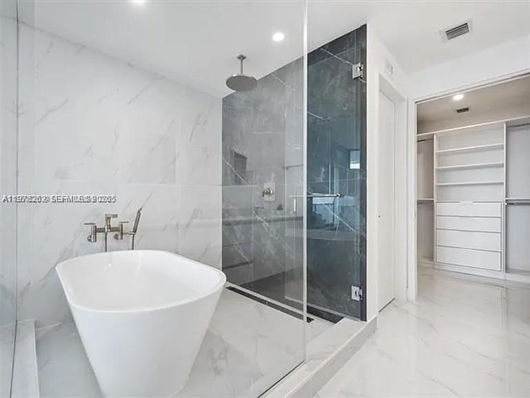 A modern bathroom features a white soaking tub, a glass-enclosed shower, and an adjacent closet — 700 NE 24TH ST # 606, Miami FL 33137, MIAMI, FL