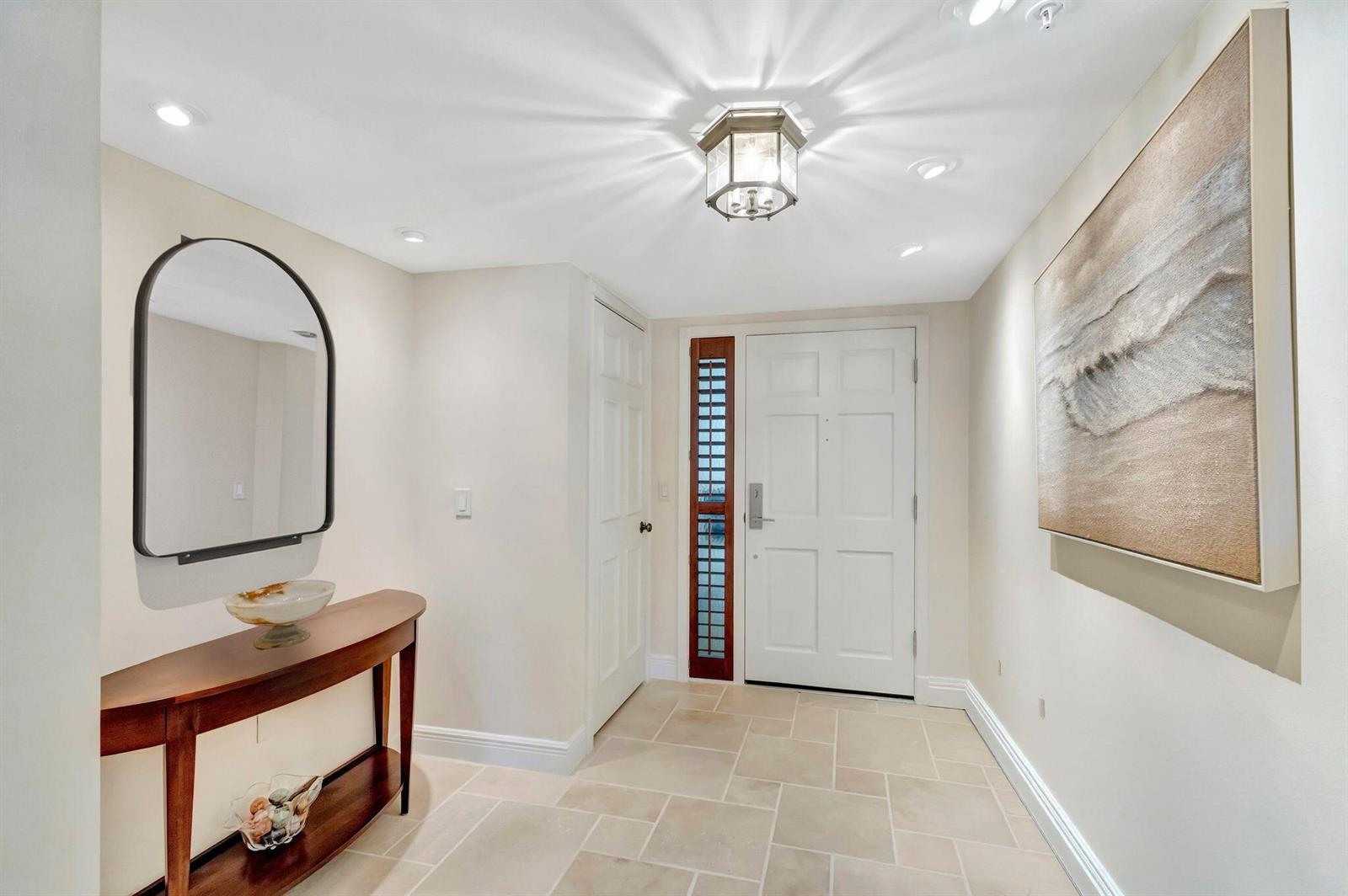 An entryway features a console table, arched mirror, tiled floor, and a white front door — 400 Beach Road # 804, Tequesta FL 33469, TEQUESTA, FL