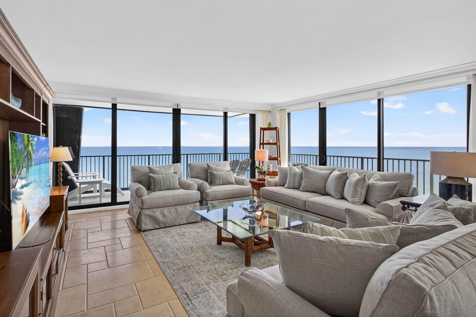 A living room with tile floors, gray furniture, and floor-to-ceiling windows overlooking the ocean — 400 Beach Road # 804, Tequesta FL 33469, TEQUESTA, FL