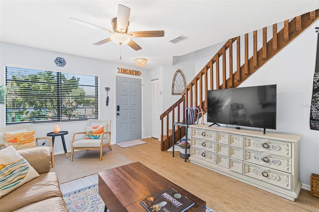 A living room features a wooden staircase, a television on a dresser, and a ceiling fan — 117 HARBOR DRIVE, CAPE CANAVERAL, FL