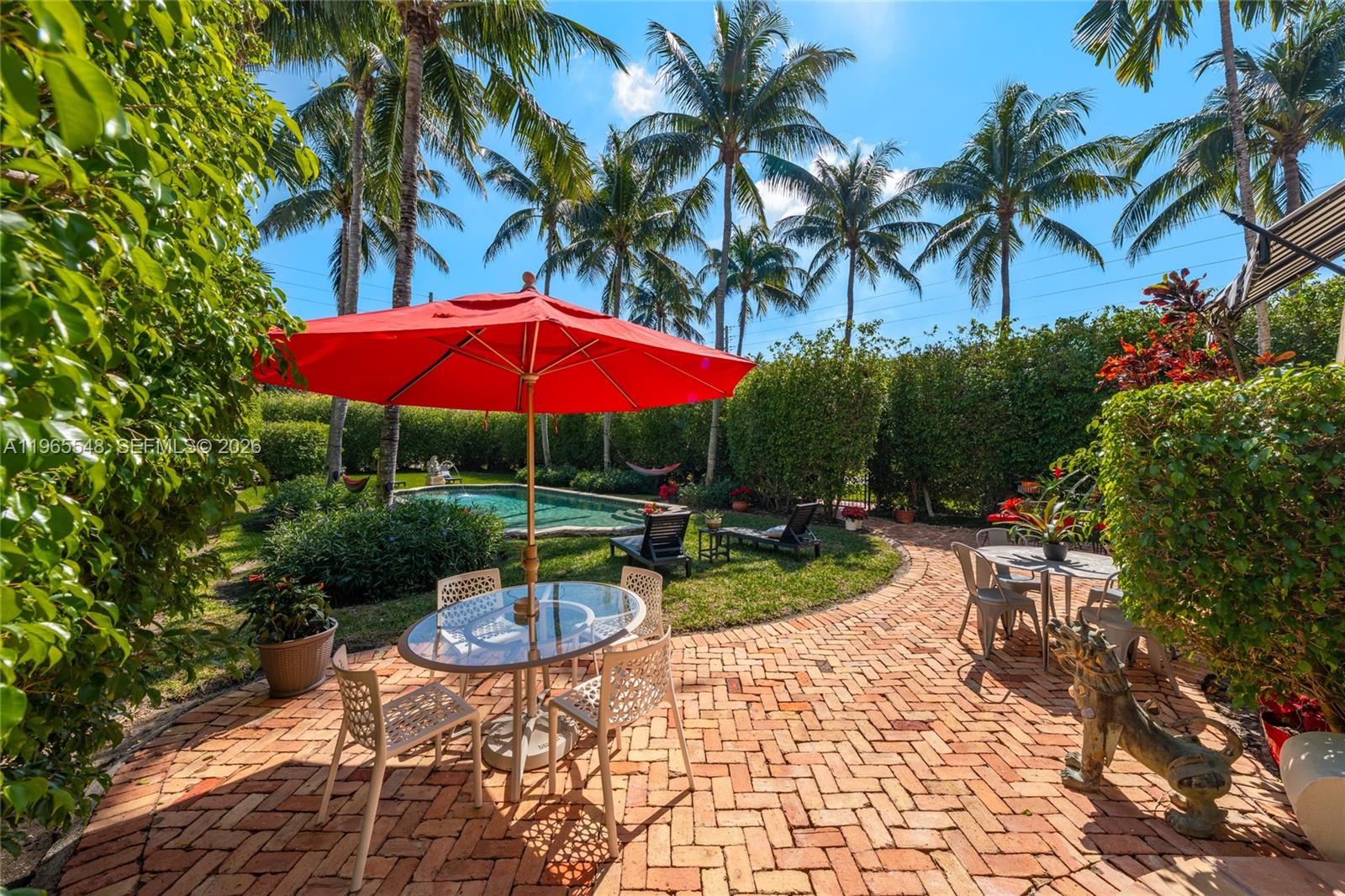 A brick patio with outdoor dining sets and a red umbrella overlooks a swimming pool — 4500 Sheridan Ave, Miami Beach FL 33140, MIAMI BEACH, FL