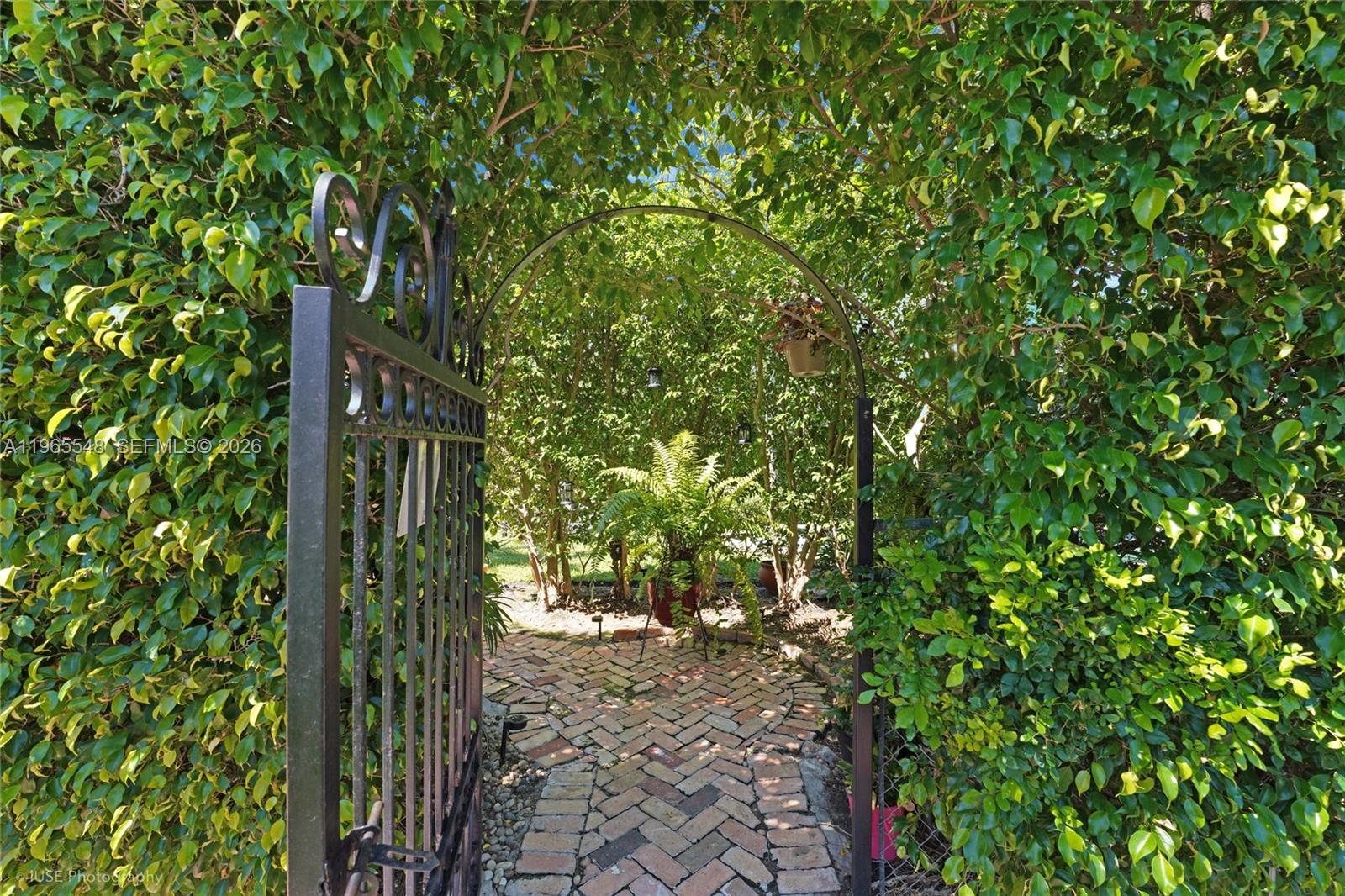 A metal gate opens onto a brick path leading through a lush, tree-lined garden archway — 4500 Sheridan Ave, Miami Beach FL 33140, MIAMI BEACH, FL