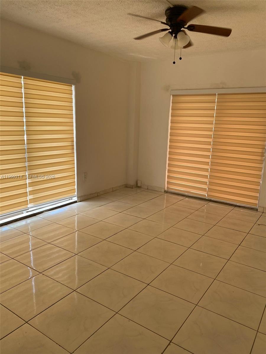An empty room features light-colored tile flooring, two windows with tan blinds, and a ceiling fan — 12500 NE 5th Ave # 101, North Miami FL 33161, NORTH MIAMI, FL