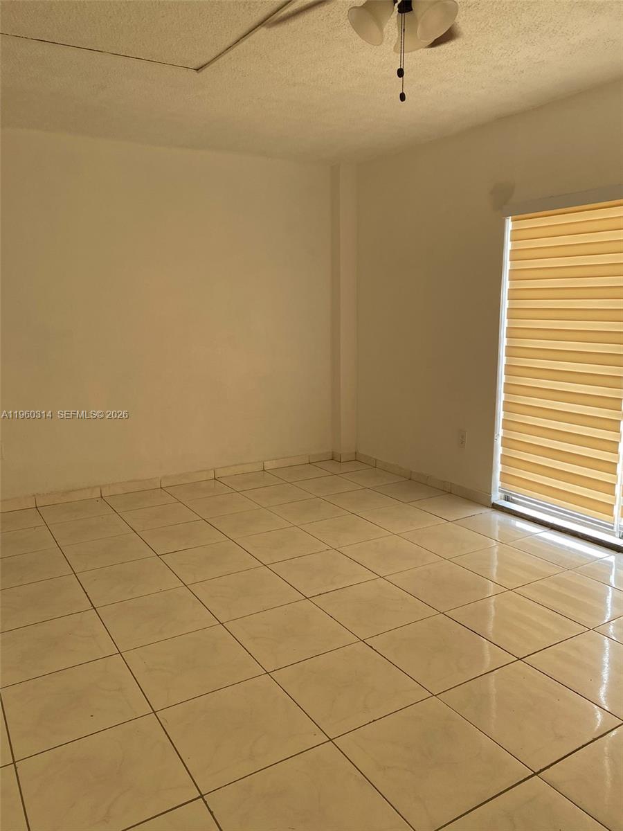 An empty room features light-colored tile flooring, white walls, and a window with blinds — 12500 NE 5th Ave # 101, North Miami FL 33161, NORTH MIAMI, FL