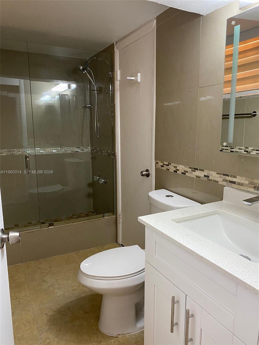 A bathroom features a glass-enclosed shower, a white vanity with a sink, and a toilet — 12500 NE 5th Ave # 101, North Miami FL 33161, NORTH MIAMI, FL
