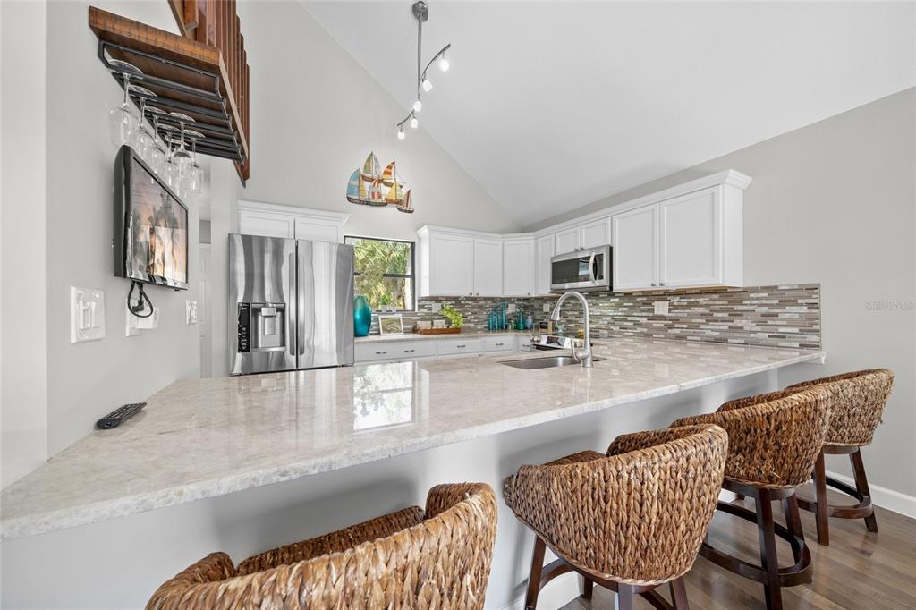 A kitchen features white cabinets, stainless steel appliances, a stone countertop, and woven bar stools — 1256 RIEGELS LANDING DRIVE, SARASOTA, FL
