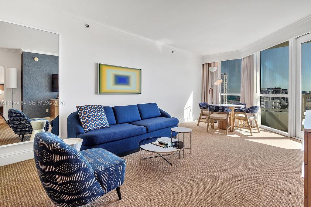 A living room features a blue sofa, patterned armchair, coffee tables, and a dining area — 4401 Collins Ave # 1712, Miami Beach FL 33140, MIAMI BEACH, FL