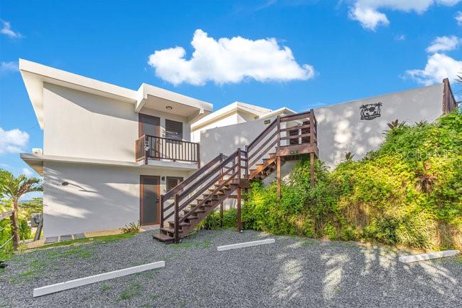 A two-story white building features an exterior wooden staircase leading to an upper balcony — COZY CASITAS-PUNTAS- CALLE VISTA DEL MAR, RINCON, PR