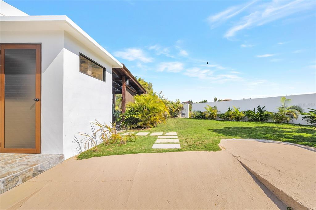 A white building with a glass door sits next to a grassy yard with pavers — COZY CASITAS-PUNTAS- CALLE VISTA DEL MAR, RINCON, PR