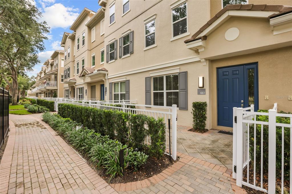 A tan three-story townhouse with a blue front door and a white picket fence — 661 HANGNEST LANE, LAKE MARY, FL