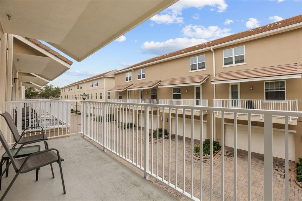 A balcony with two chairs overlooks a paved courtyard between rows of tan townhouses — 661 HANGNEST LANE, LAKE MARY, FL