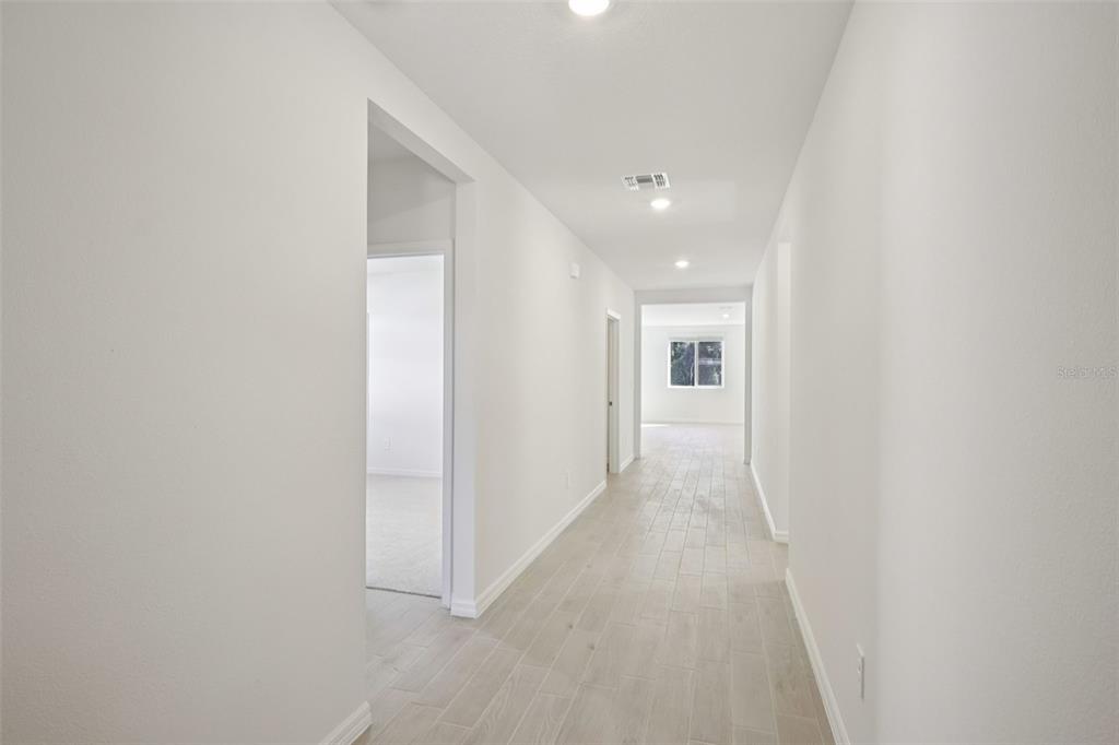 A bright hallway with light-colored tile flooring leads toward a window at the far end — 7200 RAY CREEK DRIVE, BROOKSVILLE, FL