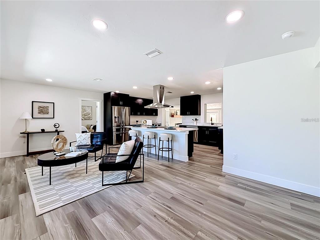 An open-concept kitchen and living area features dark cabinetry, a central island, and wood-look flooring — 2335 MURILLA WAY S, ST PETERSBURG, FL