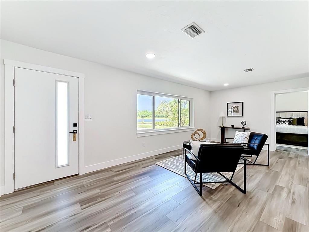 A living room with light wood-look flooring, two black chairs, and a view of water — 2335 MURILLA WAY S, ST PETERSBURG, FL