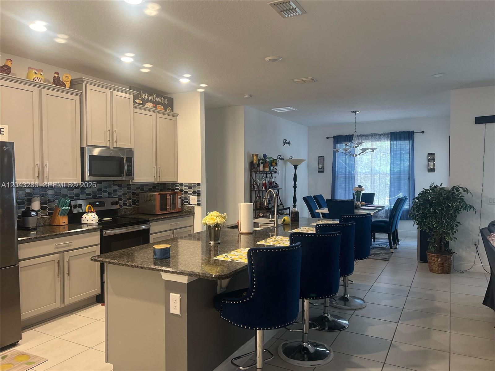 A kitchen with gray cabinets, a granite island, and blue bar stools faces a dining area — 3855 Carrick Bend Dr, Kissimmee FL 34746, KISSIMMEE, FL