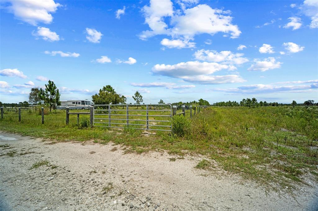 A metal gate opens into a grassy, fenced field under a bright blue sky — 49021 BERMONT ROAD, PUNTA GORDA, FL