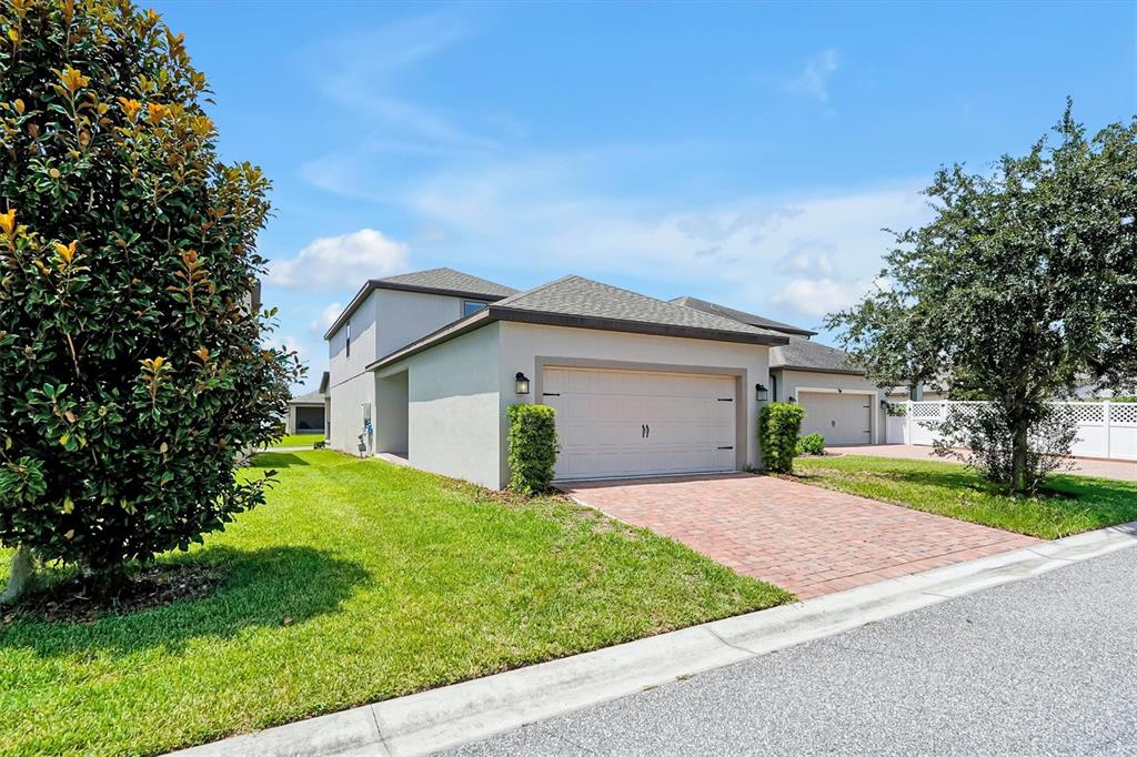 A light-colored house with a brick driveway and a two-car garage under a blue sky — 15101 PURPLE MARTIN STREET, WINTER GARDEN, FL