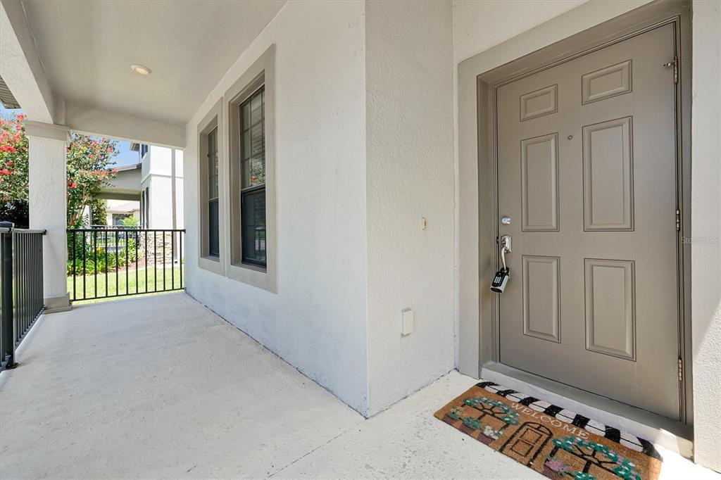 A covered porch features a gray front door with a lockbox and a welcome mat — 15101 PURPLE MARTIN STREET, WINTER GARDEN, FL