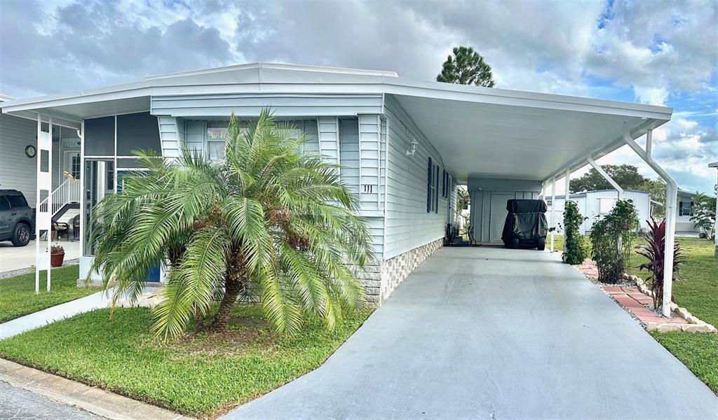 A light blue mobile home features a large palm tree and a covered carport — 9790 66TH STREET UNIT 111, PINELLAS PARK, FL