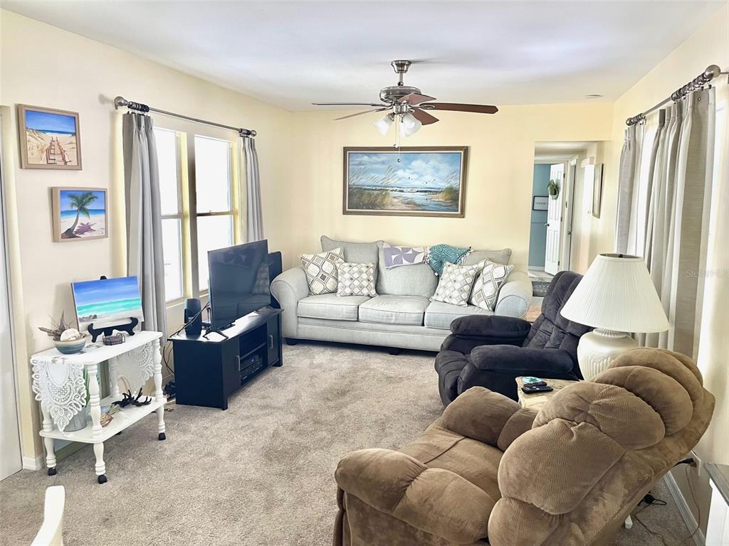 A living room features a grey sofa, two recliners, a television, and beige carpeting — 9790 66TH STREET UNIT 111, PINELLAS PARK, FL