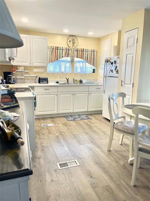 A kitchen features white cabinets, light wood-look flooring, and a small dining area — 9790 66TH STREET UNIT 111, PINELLAS PARK, FL