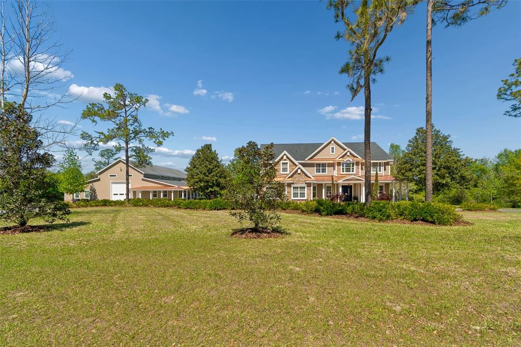 A large two-story house with a detached garage sits on a grassy, tree-lined lot — 32641 BLUEBERRY HILL WAY, DADE CITY, FL