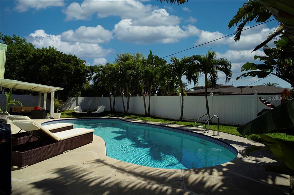 A backyard features a kidney-shaped swimming pool, lounge chairs, palm trees, and a white fence — 2403 W VINA DEL MAR BOULEVARD, ST PETE BEACH, FL
