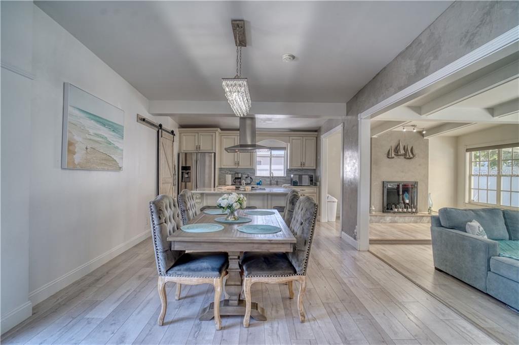 A dining area with a wooden table and tufted chairs opens to a kitchen and living room — 2403 W VINA DEL MAR BOULEVARD, ST PETE BEACH, FL