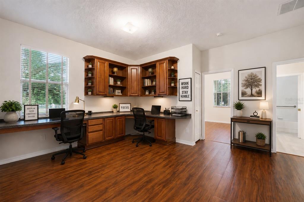 A home office features a large corner desk with built-in wooden cabinetry and wood flooring — 597 SAND WEDGE LOOP, APOPKA, FL
