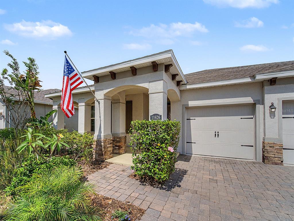 A single-story house exterior features a stone-accented entryway, a paved driveway, and an American flag — 11626 LAKE LUCAYA DRIVE, RIVERVIEW, FL