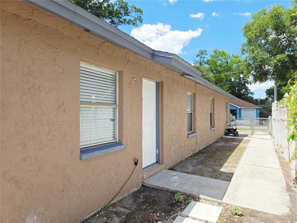 The exterior of a tan stucco building features a white door, windows, and a walkway — 1617 E IDELL STREET, TAMPA, FL