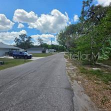 A paved residential street leads toward houses under a blue sky with scattered clouds — 8869 E OGDEN LANE, FLORAL CITY, FL