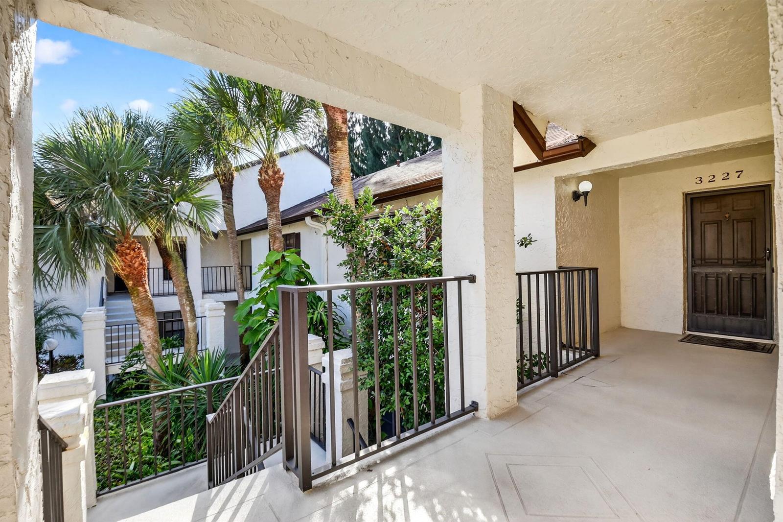 An outdoor covered walkway leads to a dark brown front door with a metal railing — 3227 Perimeter Drive, FL 33467, FL