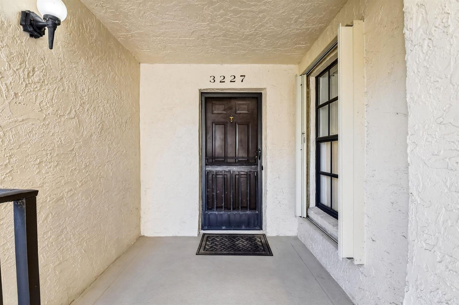 A covered entryway features a dark wooden door, a window, and a concrete floor — 3227 Perimeter Drive, FL 33467, FL