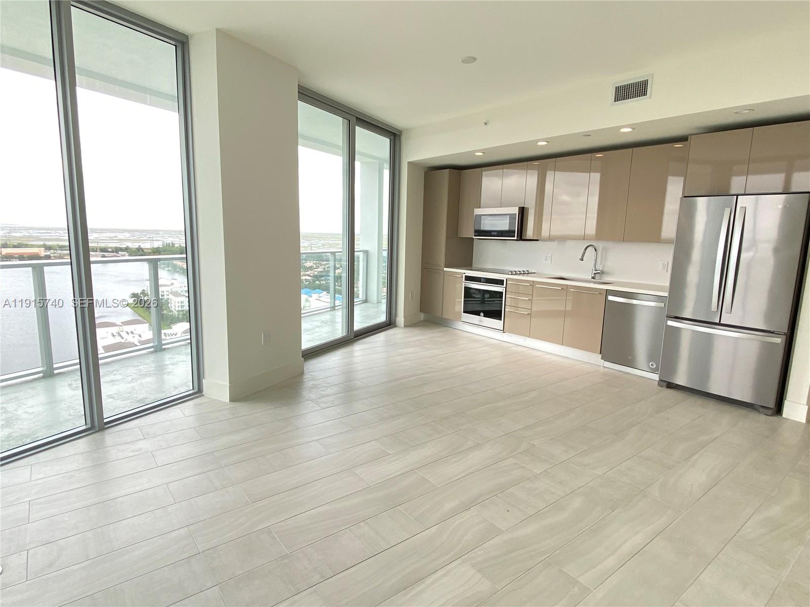A modern kitchen with glossy beige cabinets and stainless steel appliances overlooks a balcony view — 2000 Metropica Way # 2104, Sunrise FL 33323, SUNRISE, FL