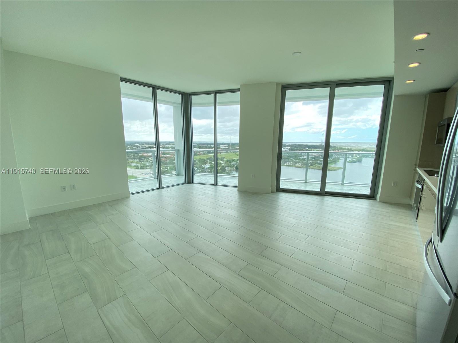 A modern living area features light-colored tile flooring, floor-to-ceiling windows, and a water view — 2000 Metropica Way # 2104, Sunrise FL 33323, SUNRISE, FL