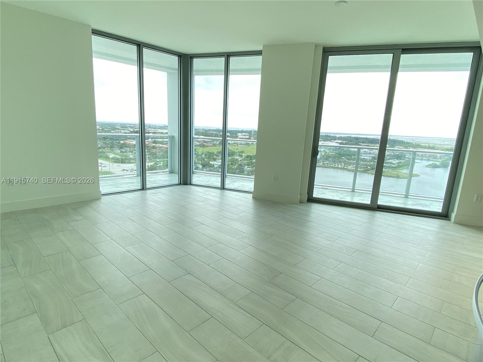 A bright, empty room features light-colored tile flooring and large floor-to-ceiling windows with balcony access — 2000 Metropica Way # 2104, Sunrise FL 33323, SUNRISE, FL