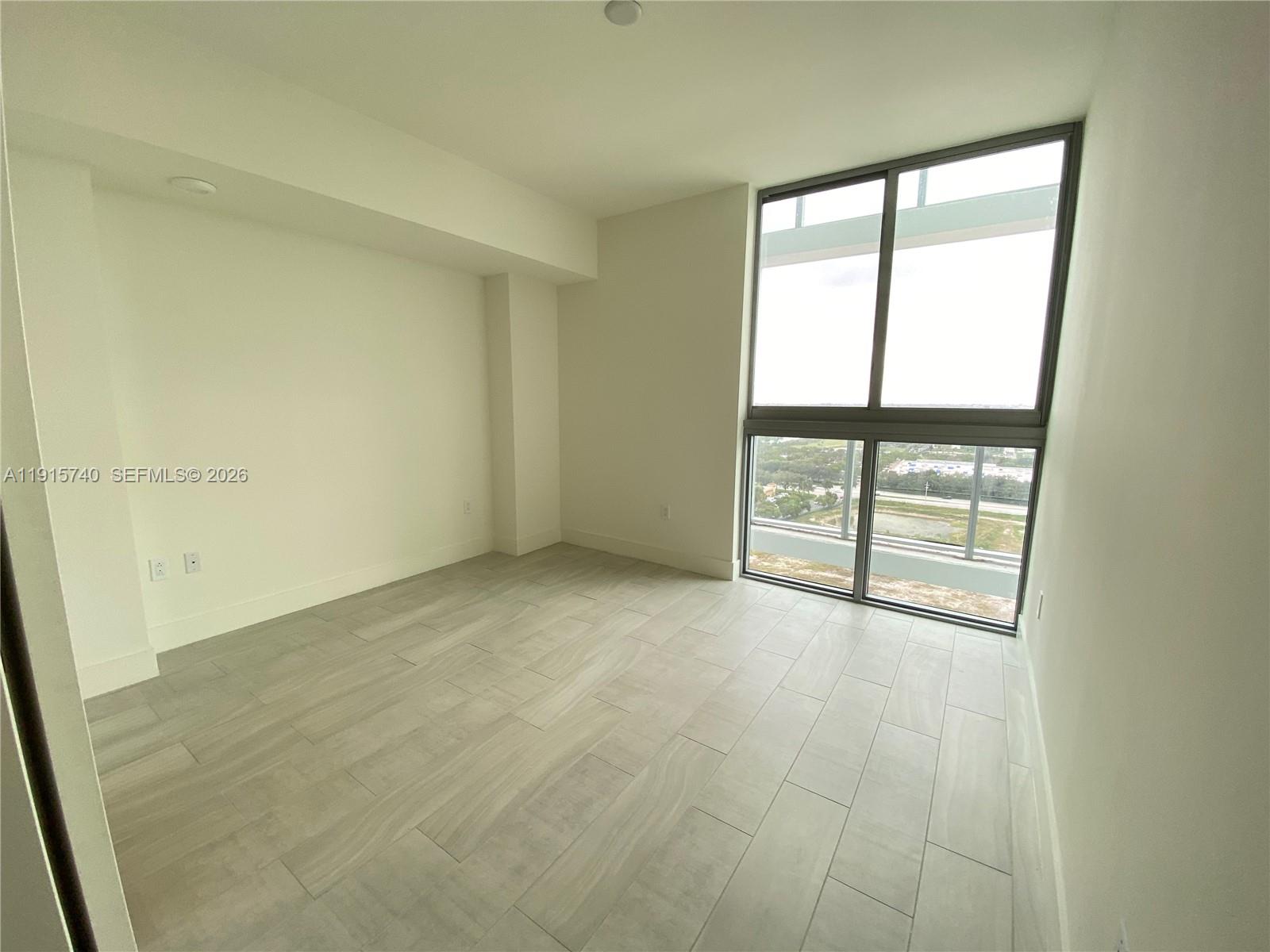 This empty room features light-colored tile flooring, white walls, and floor-to-ceiling windows — 2000 Metropica Way # 2104, Sunrise FL 33323, SUNRISE, FL