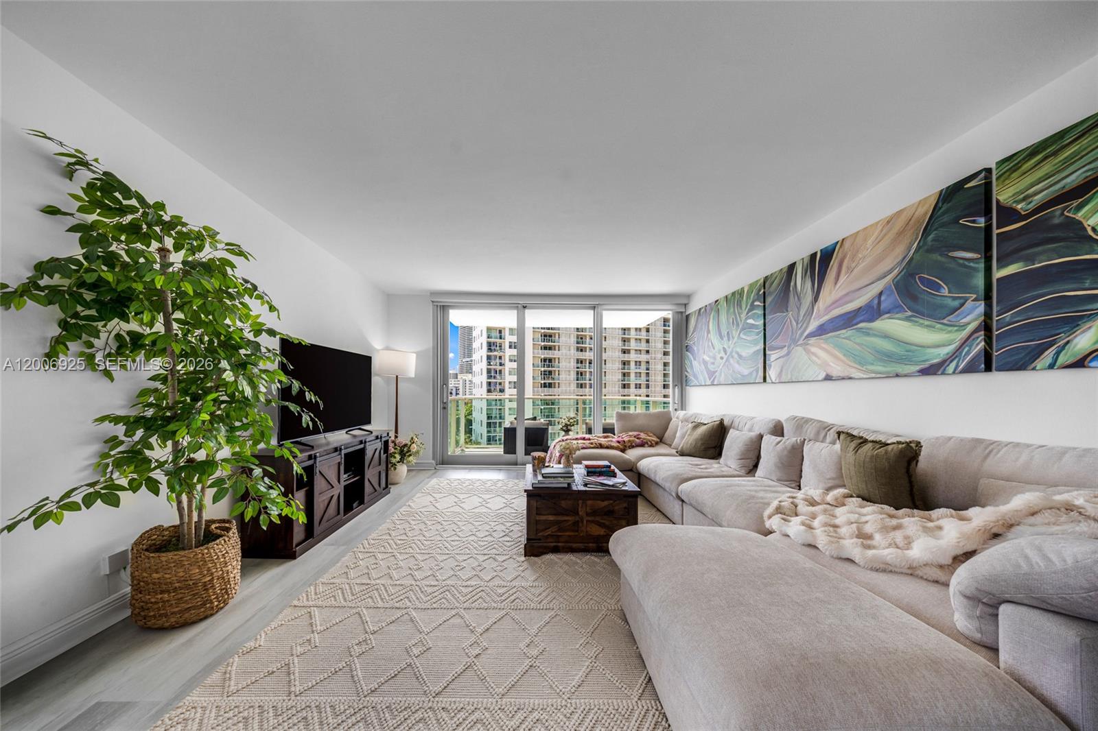 A living room features a large sectional sofa, a patterned rug, and a potted plant — 1000 West Ave # 702, Miami Beach FL 33139, MIAMI BEACH, FL