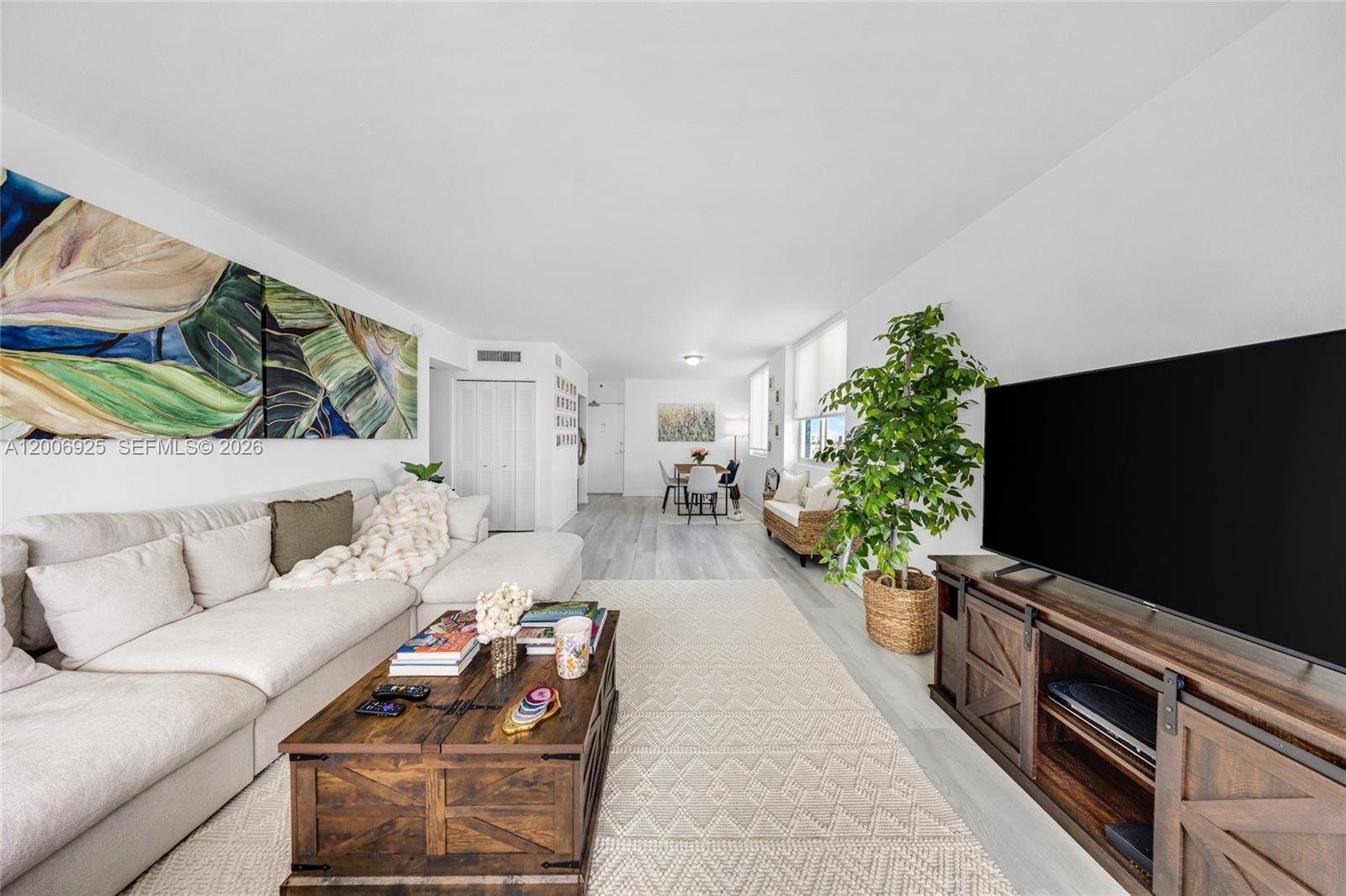 A living room features a sectional sofa, wooden coffee table, television console, and a large plant — 1000 West Ave # 702, Miami Beach FL 33139, MIAMI BEACH, FL