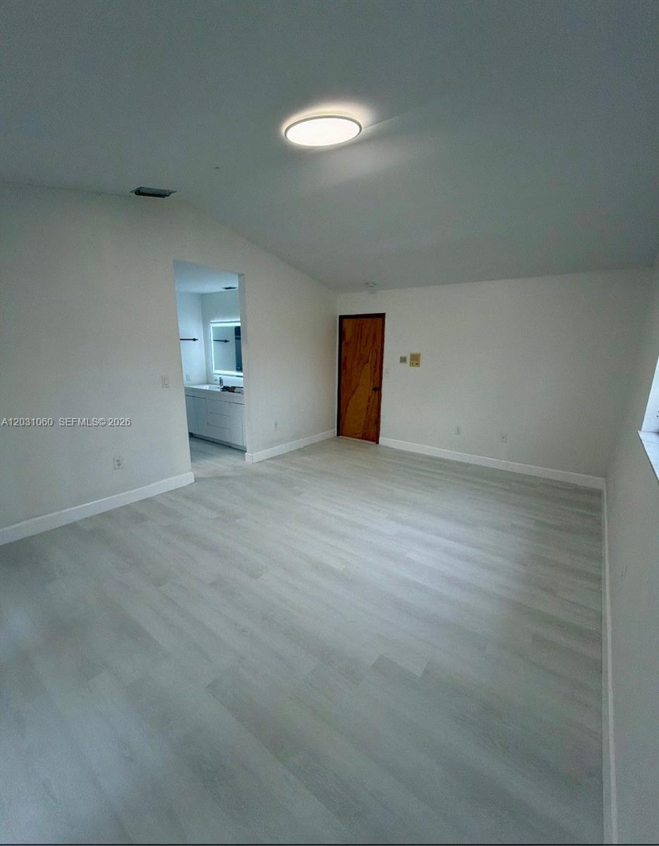 An empty bedroom features light-colored wood-look flooring, white walls, and a doorway leading to a bathroom — 18145 NW 61st Ave, Hialeah FL 33015, HIALEAH, FL