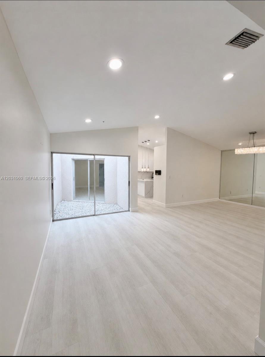 A bright living area features light wood-look flooring, recessed lighting, and a sliding glass door — 18145 NW 61st Ave, Hialeah FL 33015, HIALEAH, FL