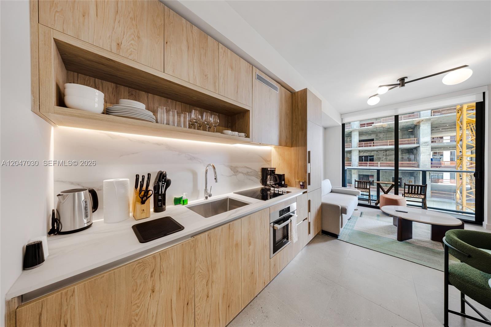 A modern kitchen with light wood cabinetry and marble countertops opens into a living area — 11 NE 6th St # 2903, Miami FL 33132, MIAMI, FL