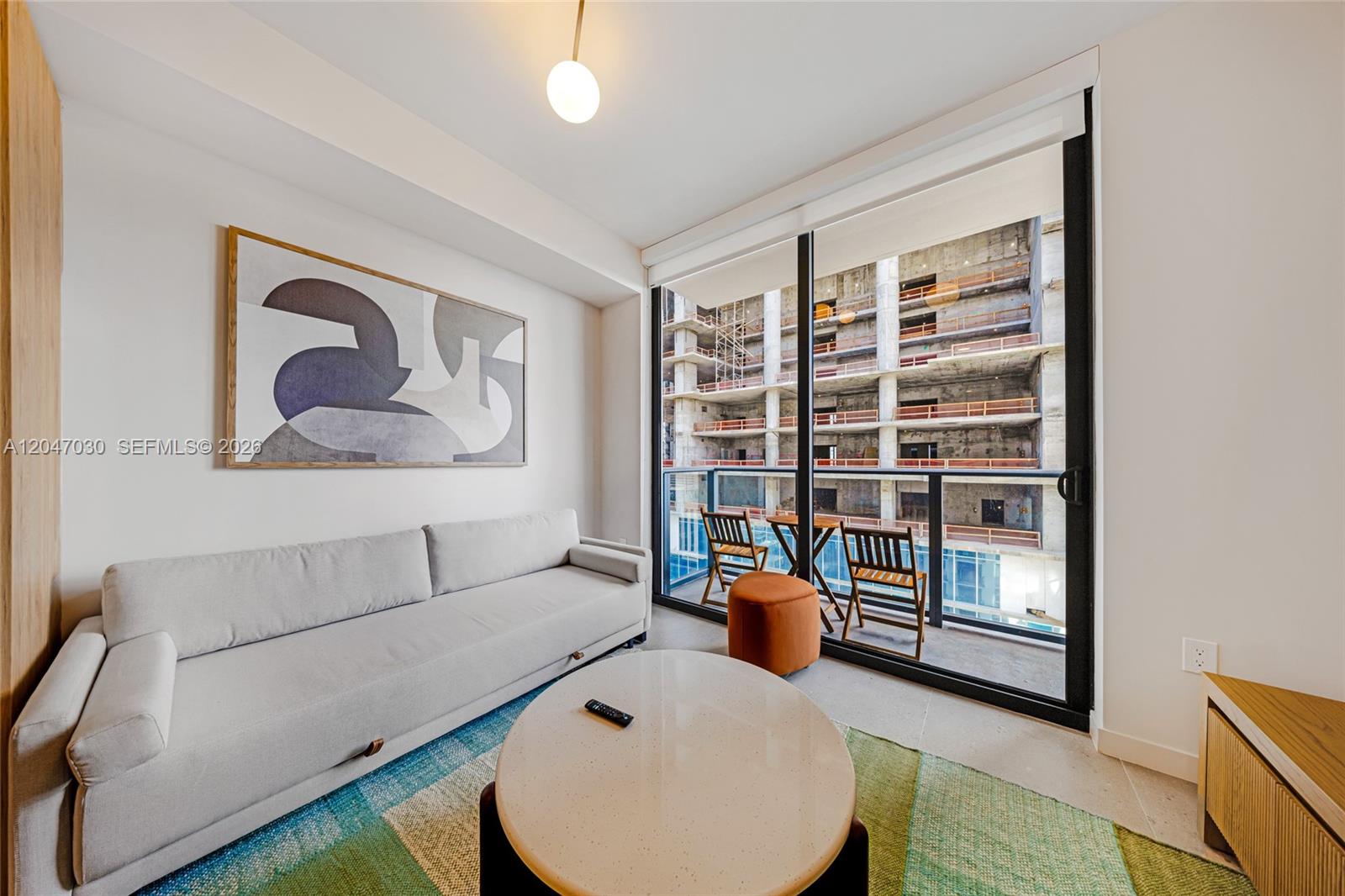 A living room features a light gray sofa, oval coffee table, and balcony overlooking construction — 11 NE 6th St # 2903, Miami FL 33132, MIAMI, FL