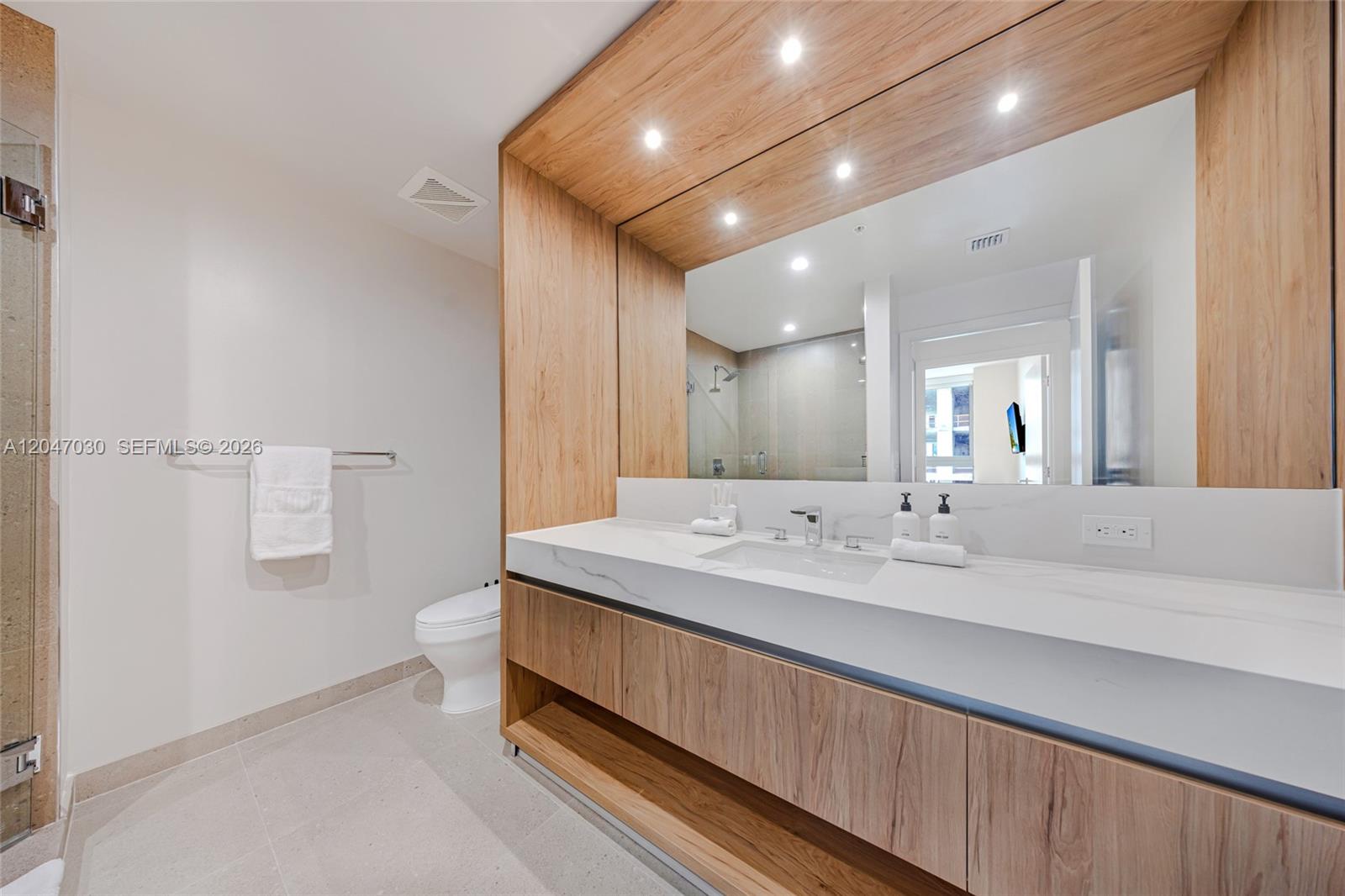 A modern bathroom features a wood-paneled vanity with a white countertop and a large mirror — 11 NE 6th St # 2903, Miami FL 33132, MIAMI, FL