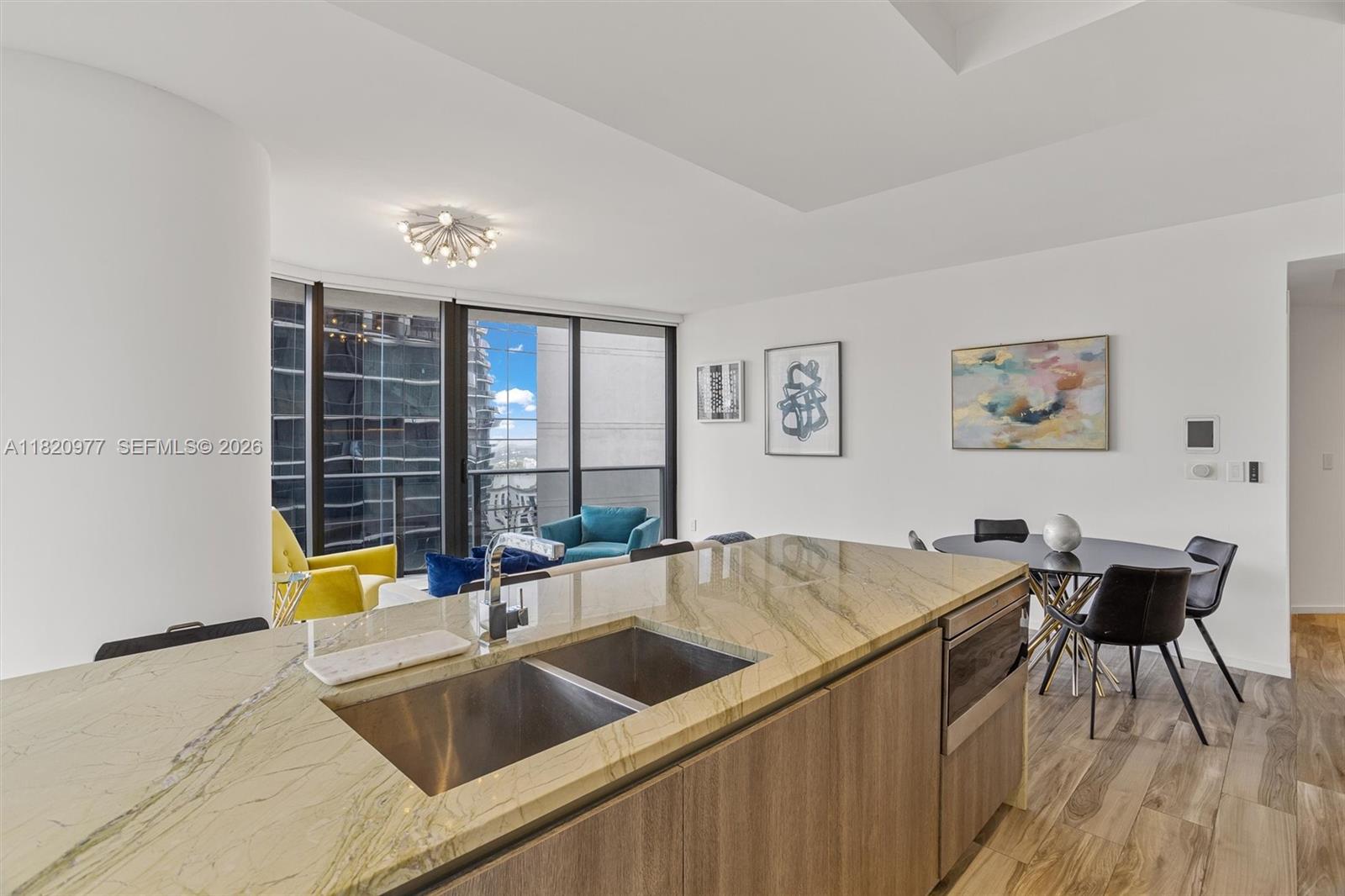 A modern kitchen with a stone island and sink overlooks a living area and balcony — 801 S Miami Ave # 4205, Miami FL 33130, MIAMI, FL