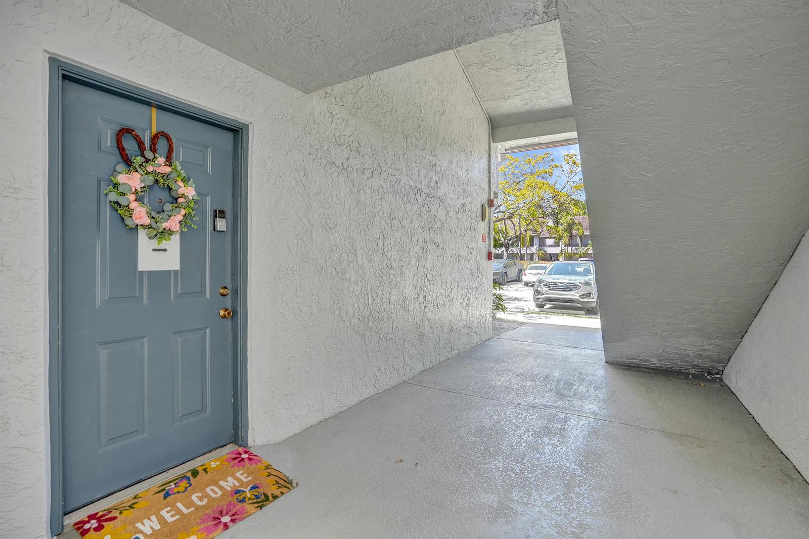 A blue front door with a floral wreath opens to a covered concrete entryway — 801 Lyons Road # 19103, Coconut Creek FL 33063, COCONUT CREEK, FL