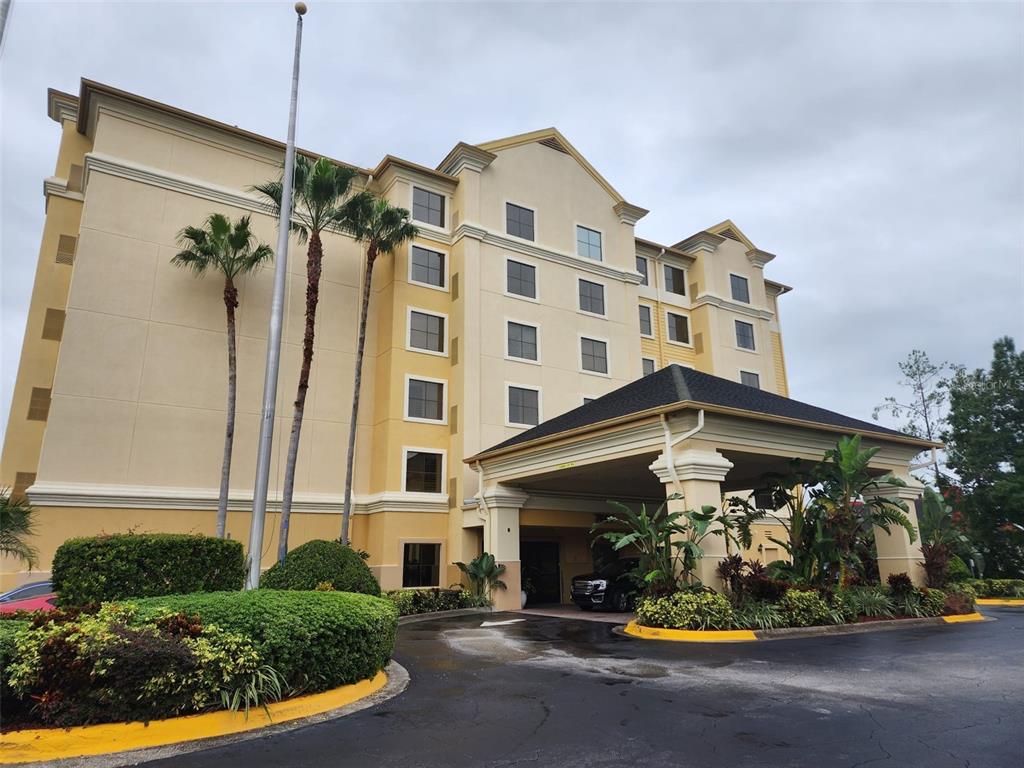 A multi-story hotel building features a covered entrance, palm trees, and landscaped shrubbery — 7601 CANADA AVENUE UNIT 418, ORLANDO, FL