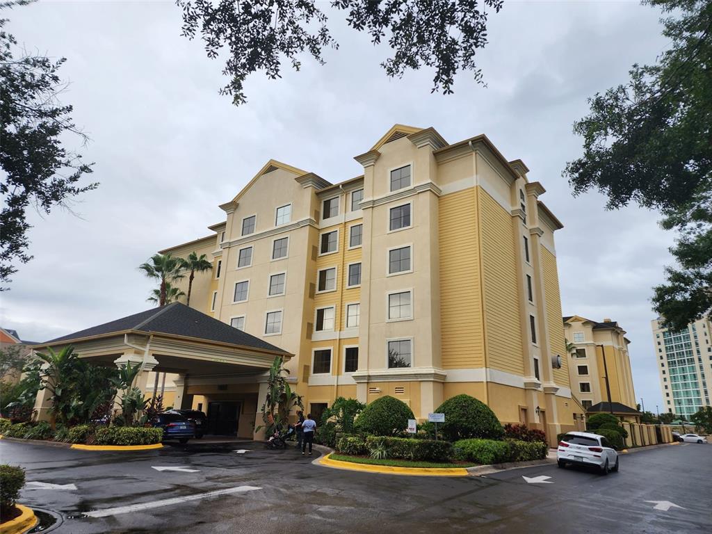 A multi-story yellow hotel building features a covered entrance and surrounding landscaping under a cloudy sky — 7601 CANADA AVENUE UNIT 418, ORLANDO, FL